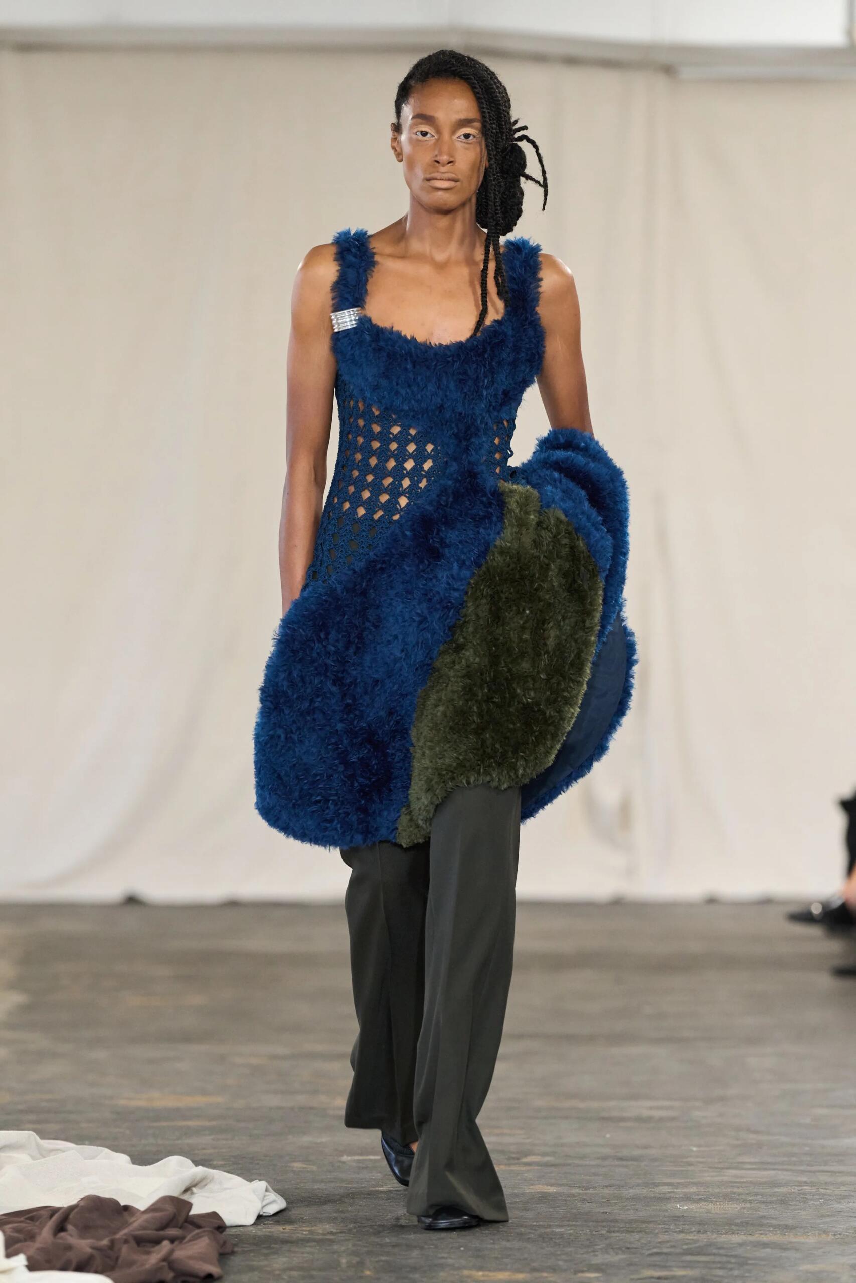 Diotima printemps-été 2027, look 1 : Volumes bleus et verts aux hanches, portés sur un pantalon de tailoring.