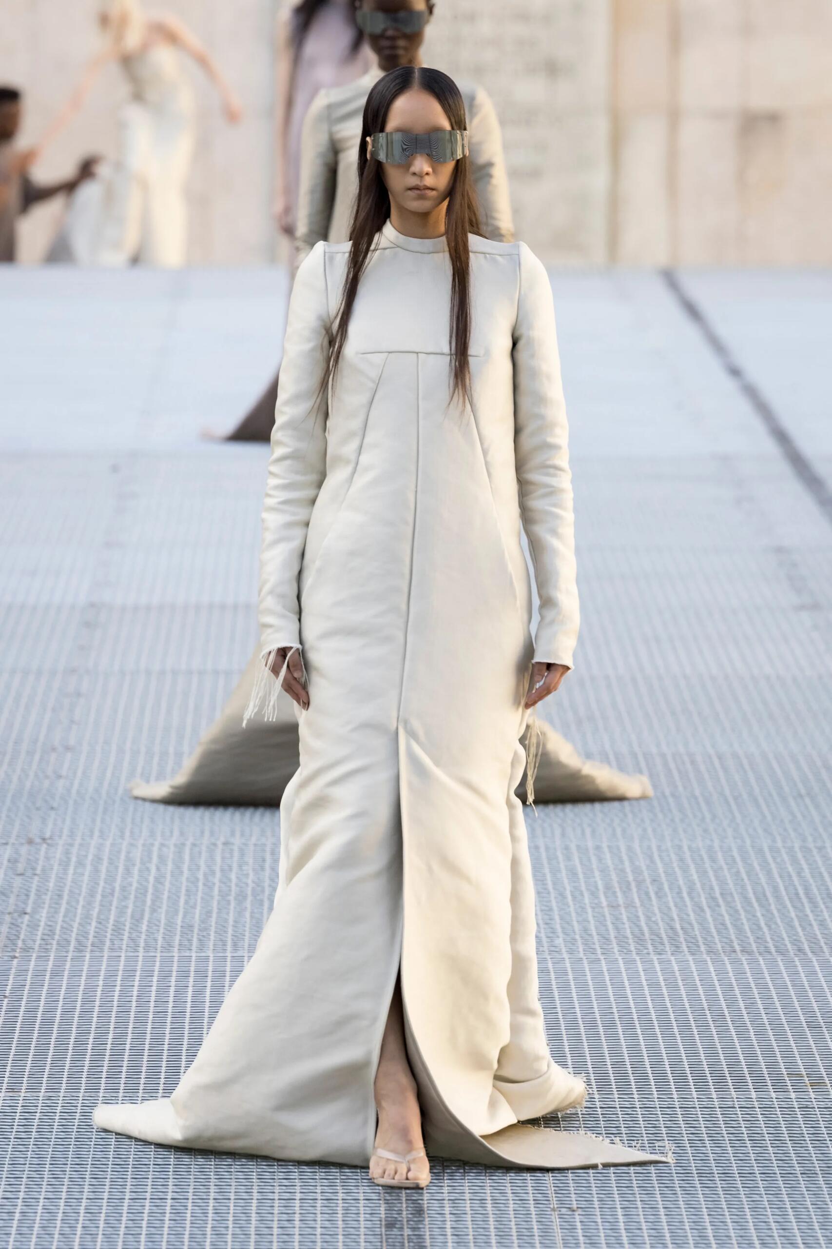 Rick Owens printemps-été 2027, look 1 : Longue silhouette cérémonielle ivoire, coutures verticales et volume structuré.