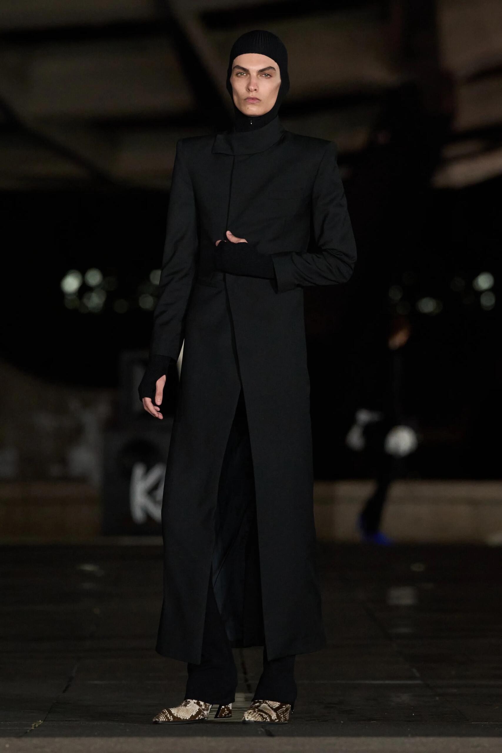 Luar printemps-été 2027, look 7 : manteau noir aux épaules tranchantes et bonnet noir.
